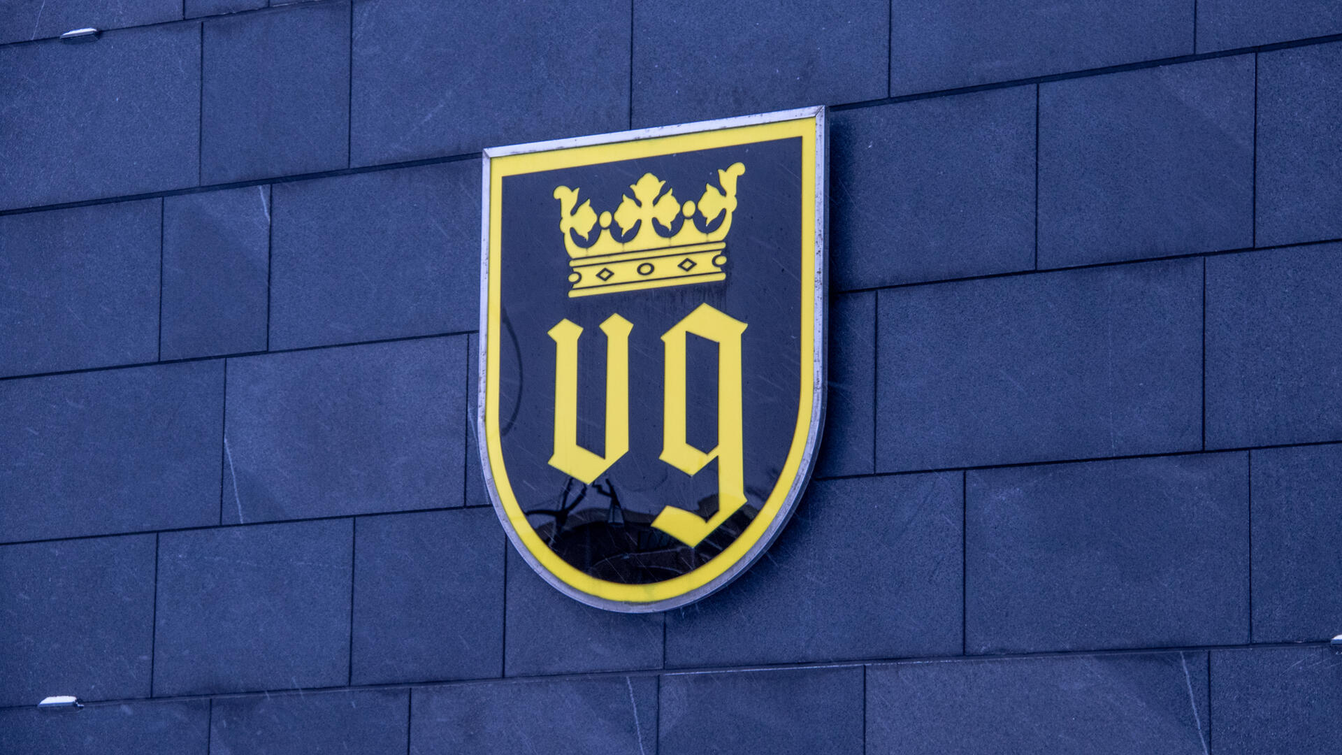 Naantalin musta-keltaisessa vaakunassa on kirjaimet VG sekä niiden yllä kruunu. Vaakuna kaupungintalon edustalla, seinässä.