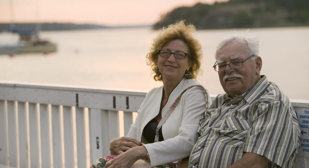 Nainen ja mies istvat vanhankaupungin rannan penkillä meri taustanaan