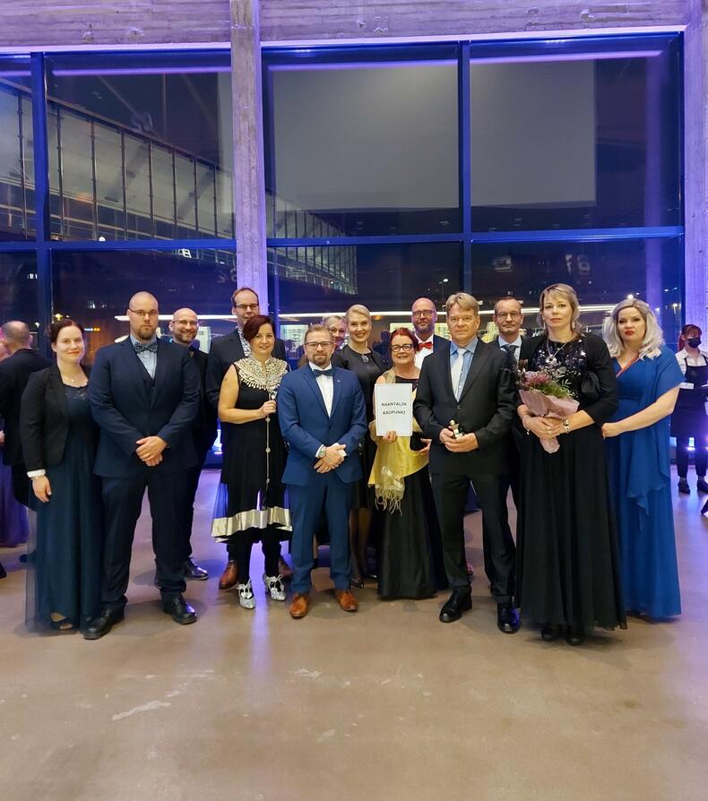 Juhlavaatteisiin pukeutuneita naantalilaisia yrittäjiä joukkona värivalaistussa salissa.