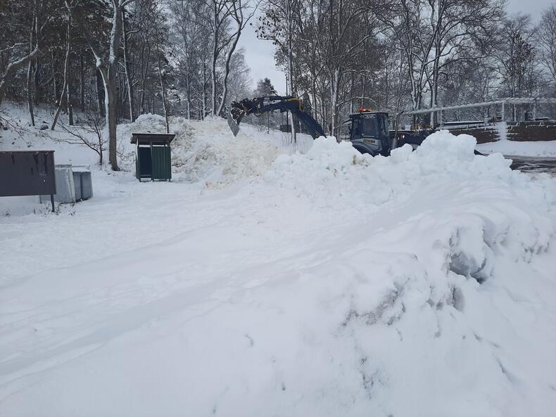 Kaivinkone tekee lumesta pulkkamäkeä.