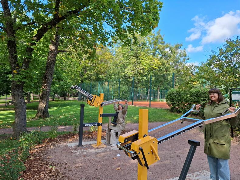 Kulttuurisuunnittelija Anu Anttila ja viestintäsuunnittelija Petra Saajanlehto käyttävät Kirkkopuiston ulkokuntolaitteita.