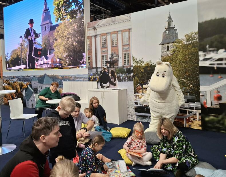 Muumipeikko ja Alma Pöysti vierailivat Naantalin osastolla matkamessuilla. Kuvassa lapsiperheitä, Alma ja Muumit.