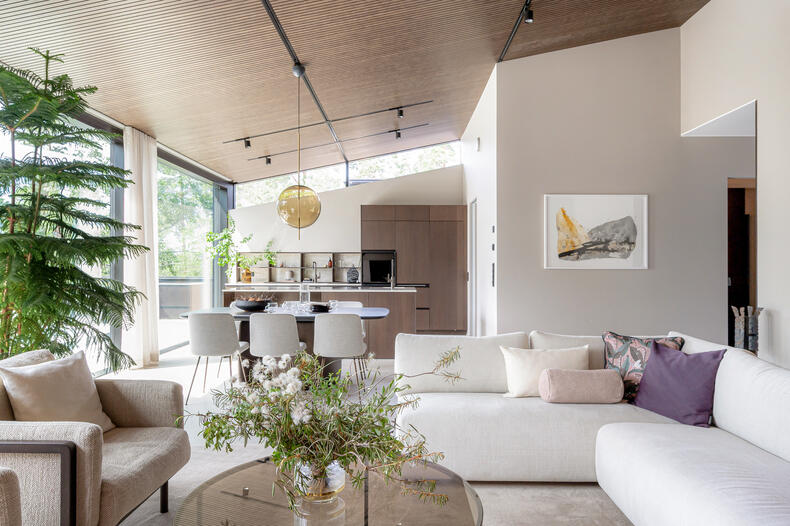 Modernisti ja vaaleilla sävyille sisustettu olohuone ja avokeittiö, jossa isot ikkunat.