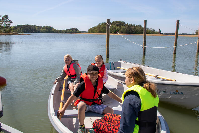 Koululaisia istuu pelastusliivit päällä soutuveneessä.