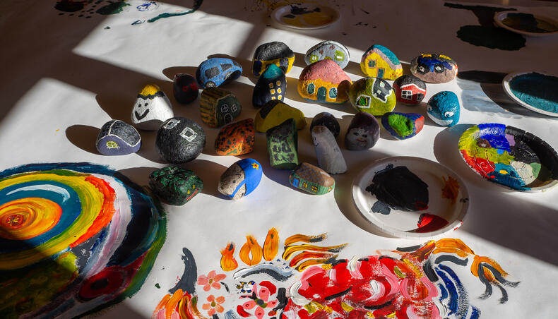 Ikkunasta heijastuu valo pöydälle, johon on koottu erilaisia värikkäästi taloiksi, autoiksi ja muiksi hahmoiksi maalattuja kiviä.