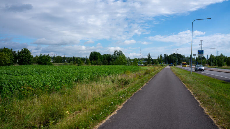 Kevyenliikenteen väylän vasemmalla puolella on auringonkukkapelto, oikealla autotie, edessä näkyy Ruonan yhdystien ja Armonlaaksintien risteys.