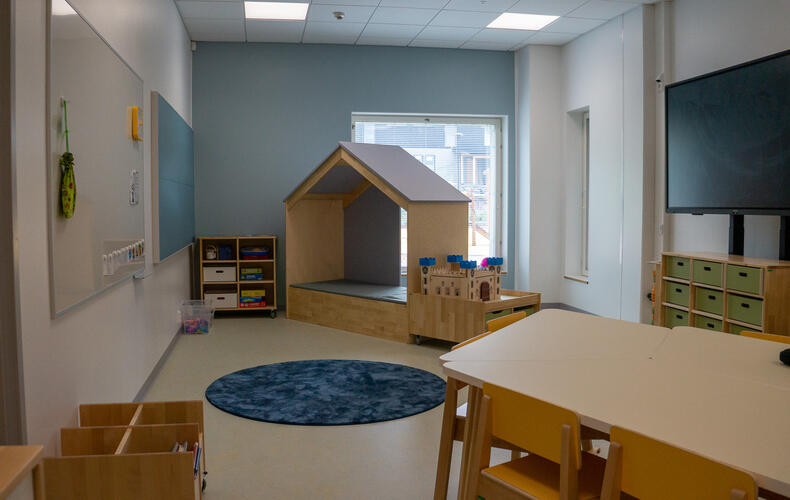 Päiväkotiluokassa talon mallinen istuin, pöytäryhmiä, näyttö.