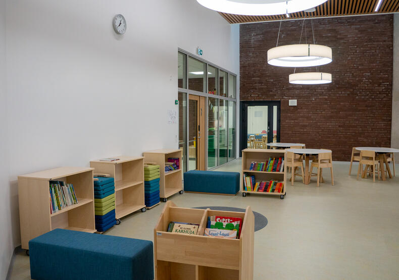 Perhetalon sisällä pienten lasten kirjastonurkkaus, takana pöytäryhmiä.