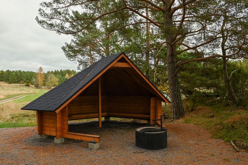 Laavu tulipaikkoineen metsän reunassa, takana peltomaisemaa.