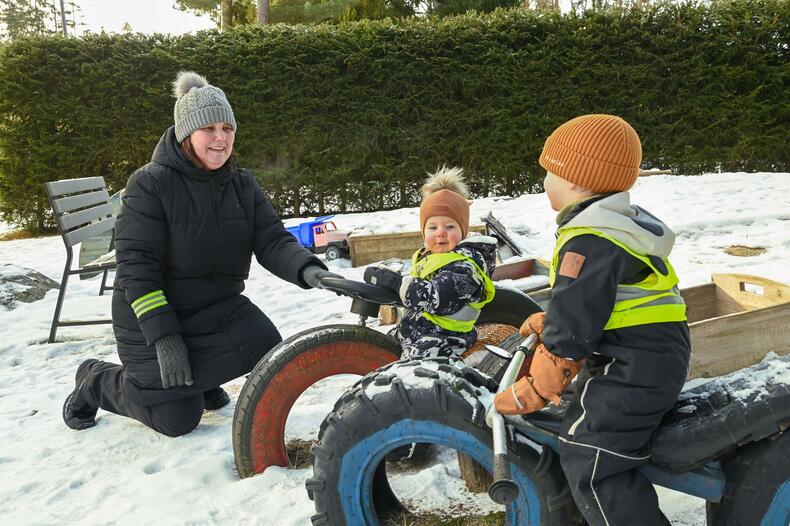 Perhepäivähoitaja leikkimässä lasten kanssa pihalla talvella.
