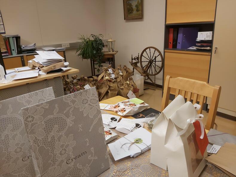 Joulupaketteja pöydällä etualalla, takana kukkia paketeissaan.