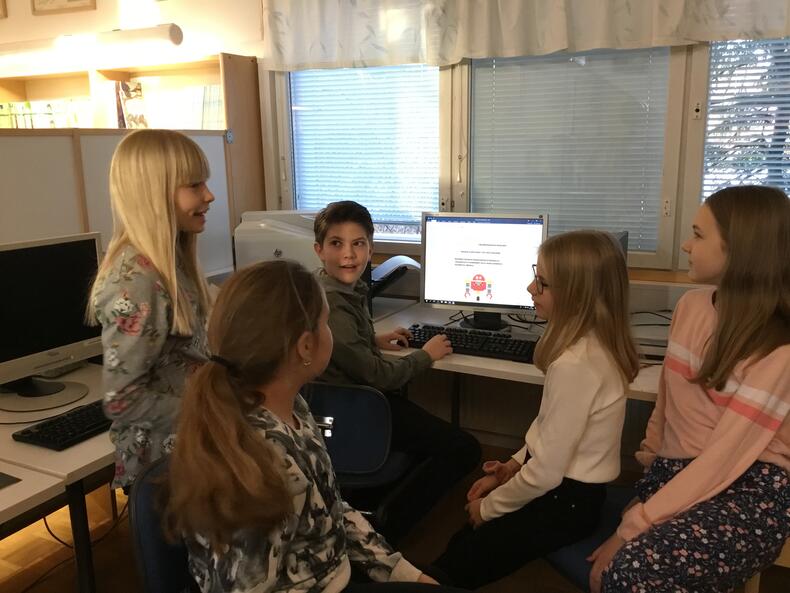 Oppilaat suunnittelevat tietokoneen ympärillä mainosta.