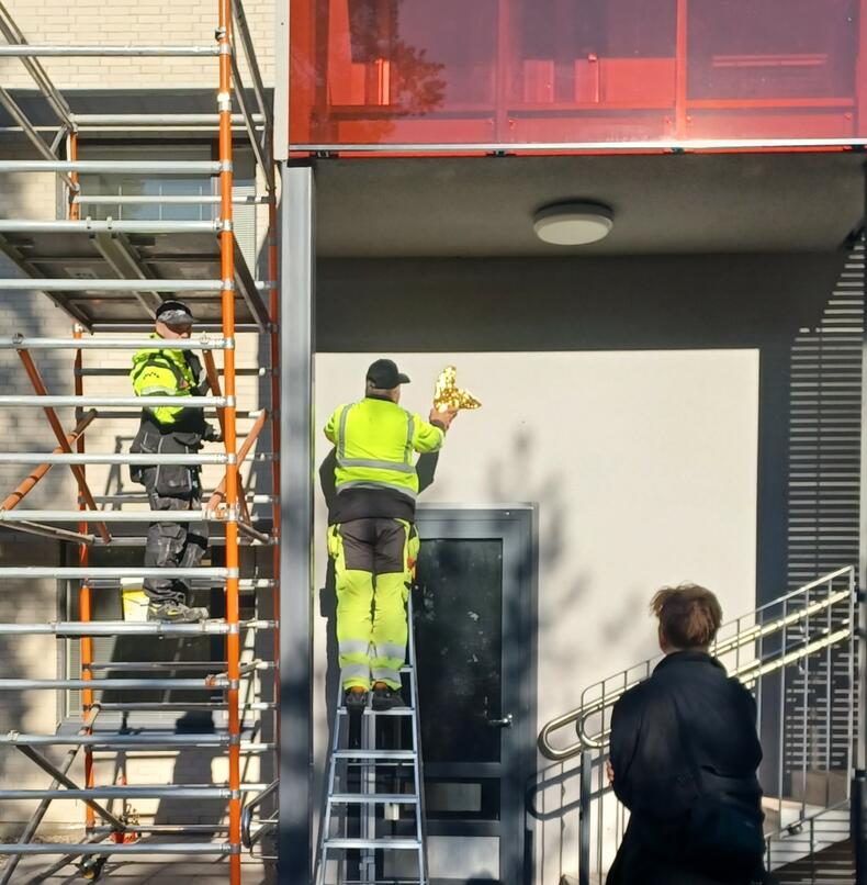 Mies kiinnittää kultaista mehiläistä Kalevanniemen seinään taiteilijan ohjaamana.