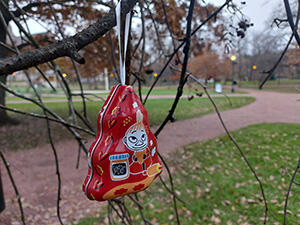 Punainen joulukuusenkoriste roikkuu puiston puun oksalla.