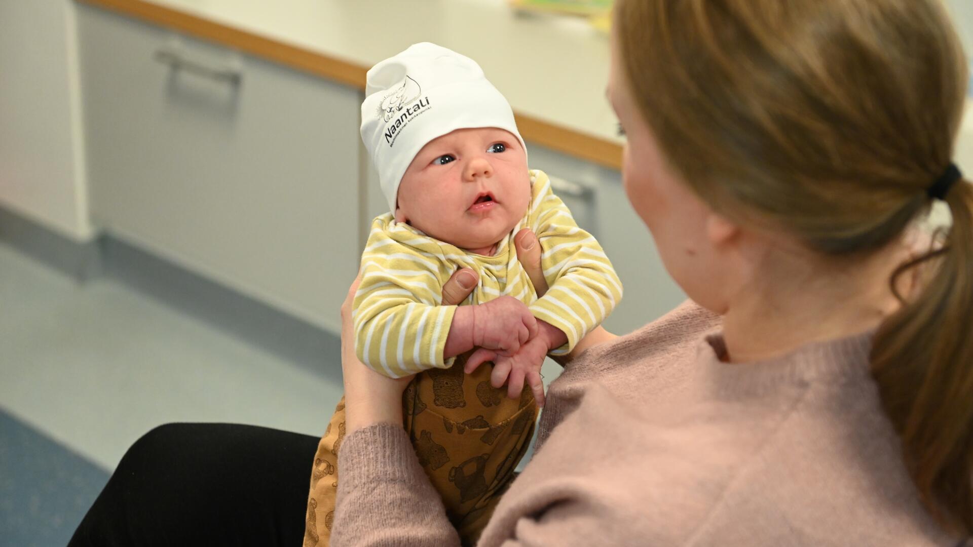 Äiti pitää sylissään lasta, jolla päässä Muumi-pipo.