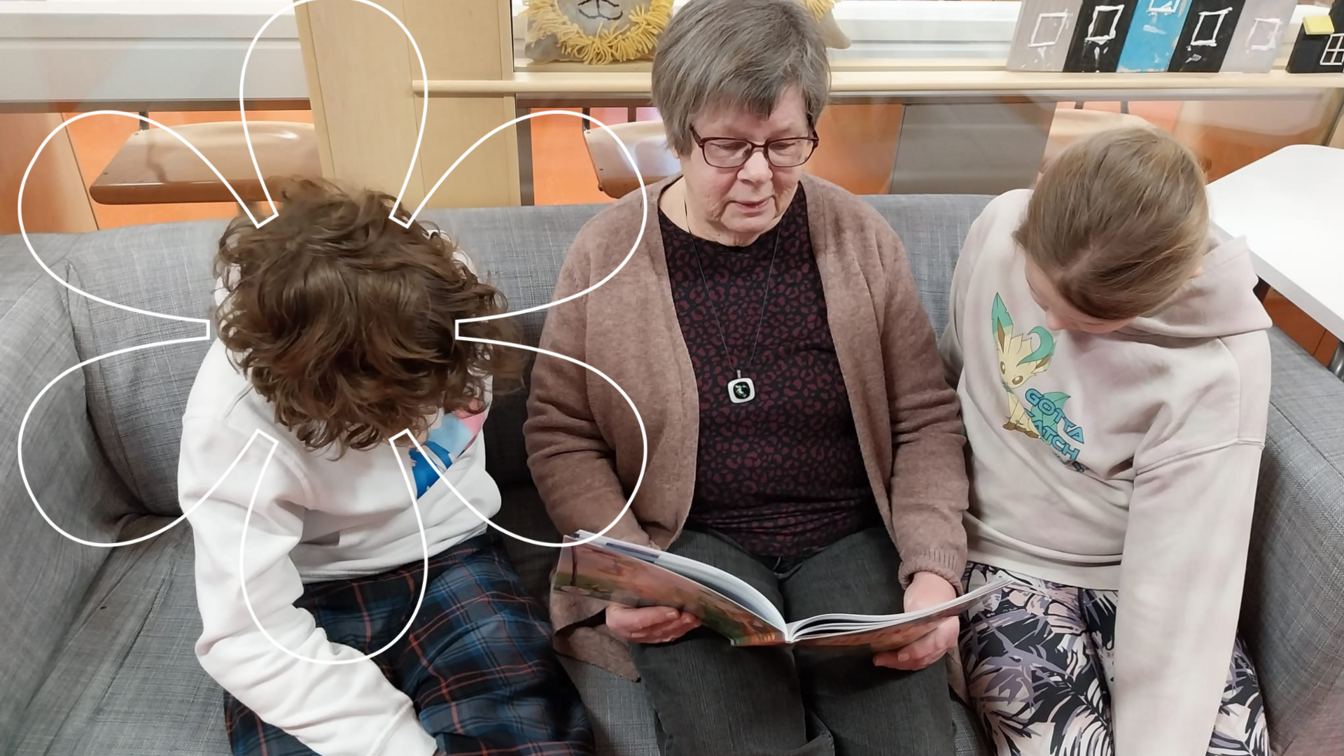 Vapaaehtoinen koulumummo lukee kahdelle oppilaalle kirjaa.