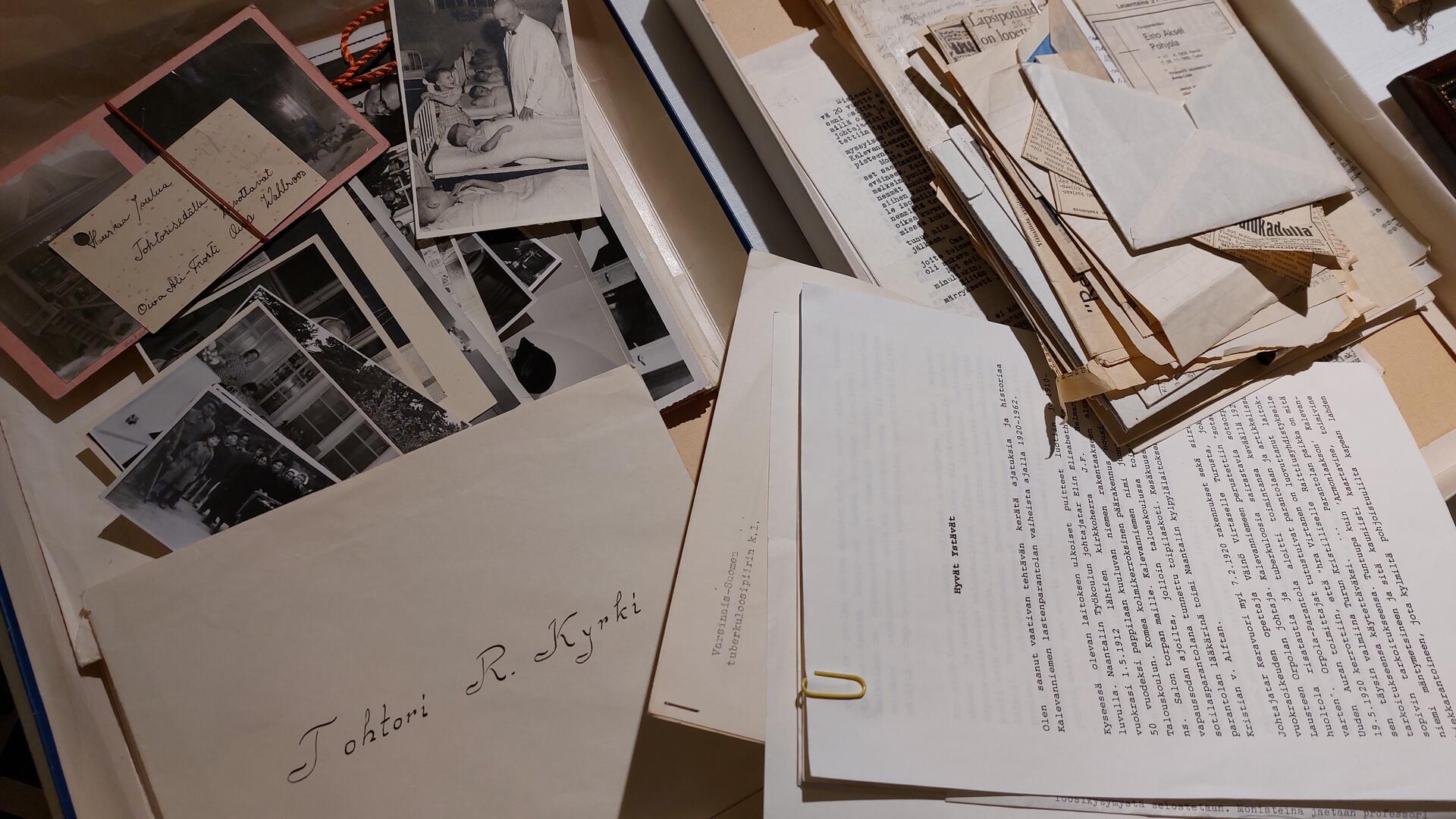 sekalaisia papereita ja mustavalkovalokuvia pöydällä