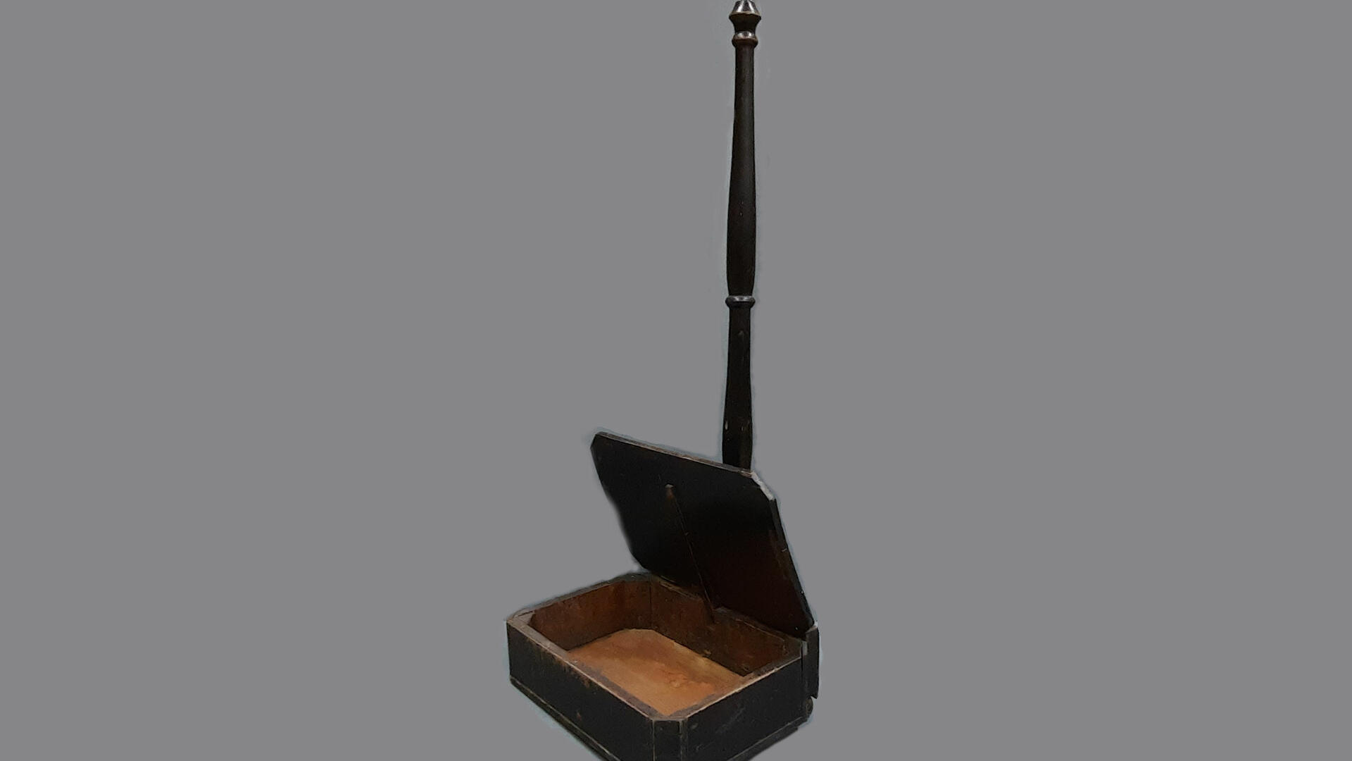 Puinen laatikko joka seisoo lattialla ja jonka takaosasta nousee ylös kapea varsi 