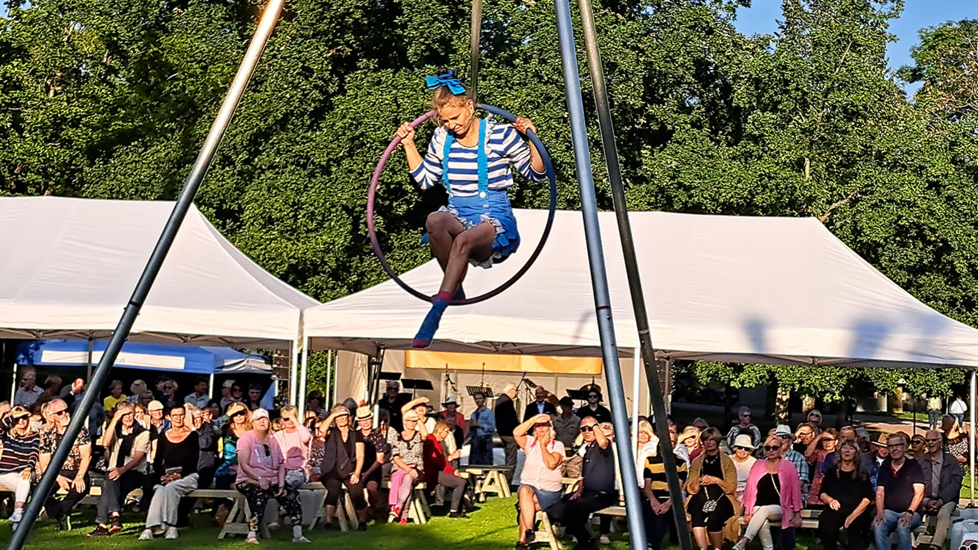 Sirkustaiteilija esiintyy trapetsilla aurinkoisessa Kirkkopuistossa.