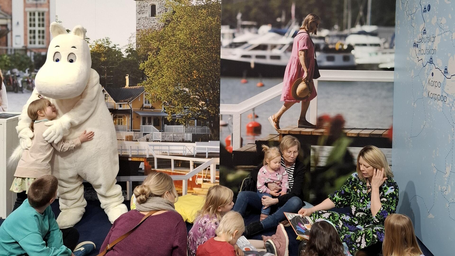 Muumipeikko ja Alma Pöysti matkamessuilla 2026 Naantalin osastolla. Kuvassa lapsia kuuntelemassa muumitarinoita.