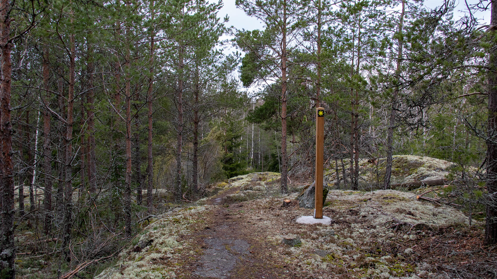 Aurinkokuvakkeella varustettu opaste kallion päällä. Keskellä kulkee polku.