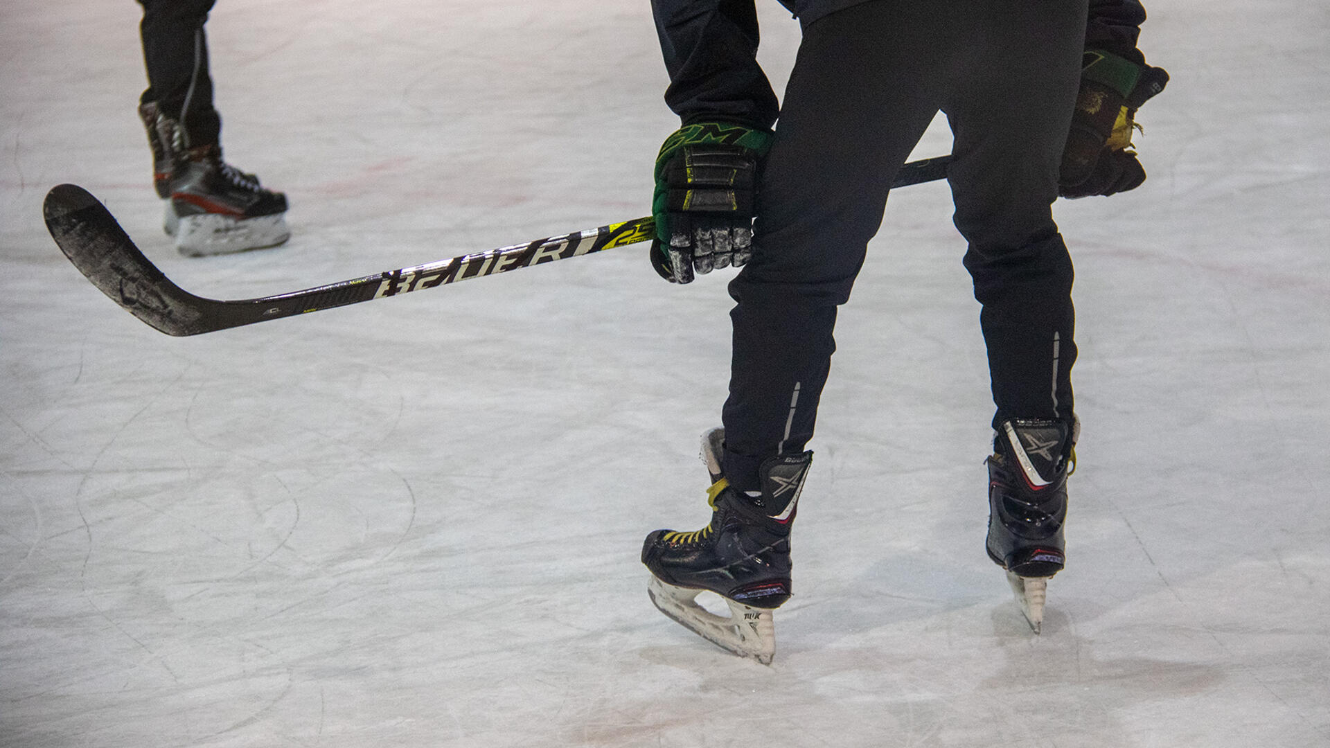 Poika on jäähallin jäällä luistelimet jalassa ja jääkiekkomaila kädessä.