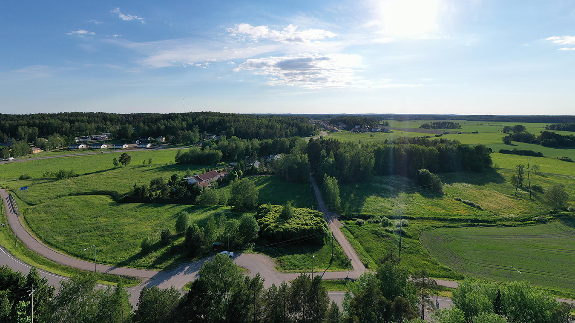 Peltoja ympärillä, etualalla ja keskellä metsää. Aurinko paistaa siniseltä taivaalta.
