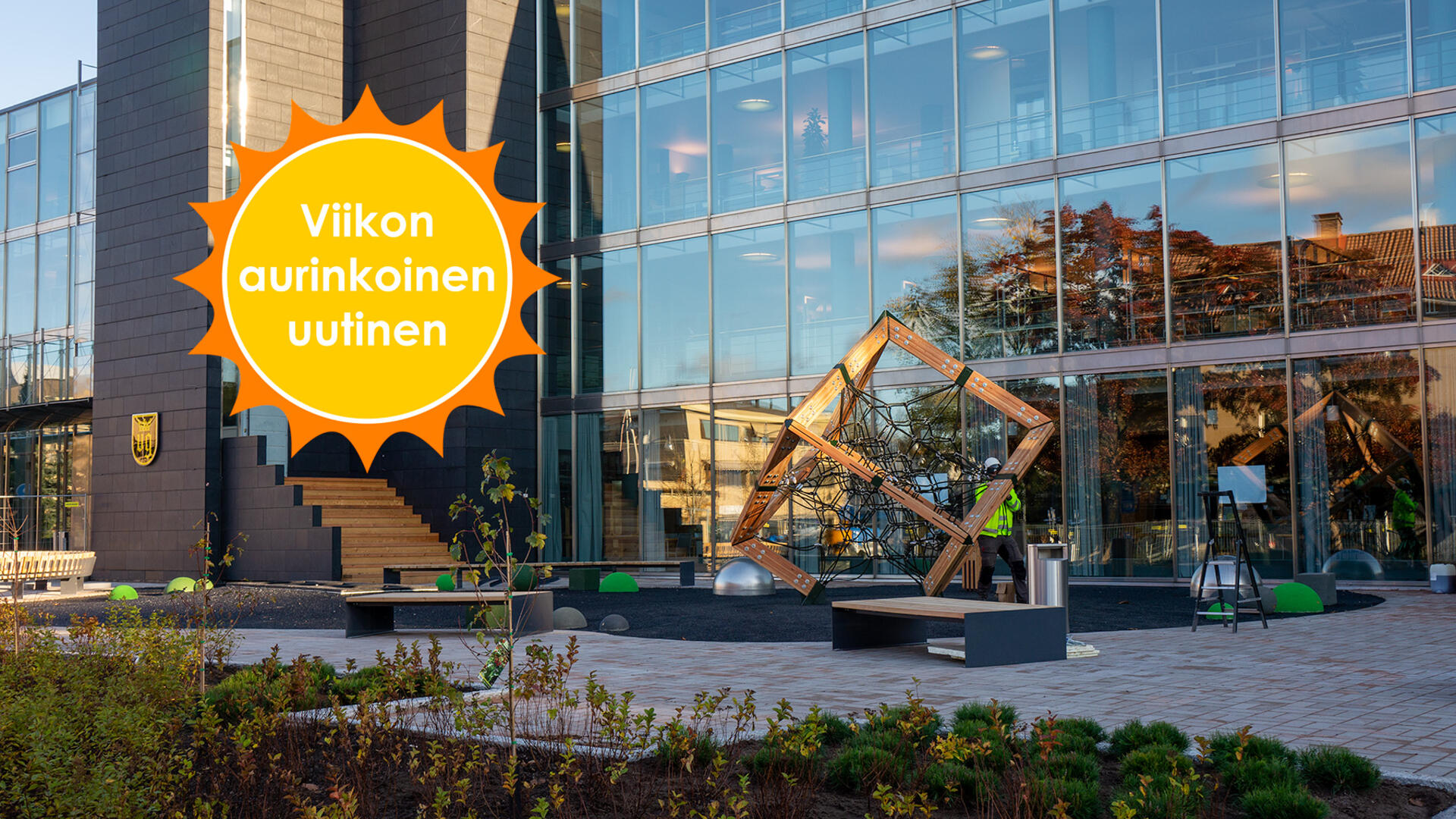 Työmies puuhaa kuutionmuotoisen kiipeilytelineen parissa Naantalin kaupungintalon edustalla. Viikon aurinkoinen uutinen