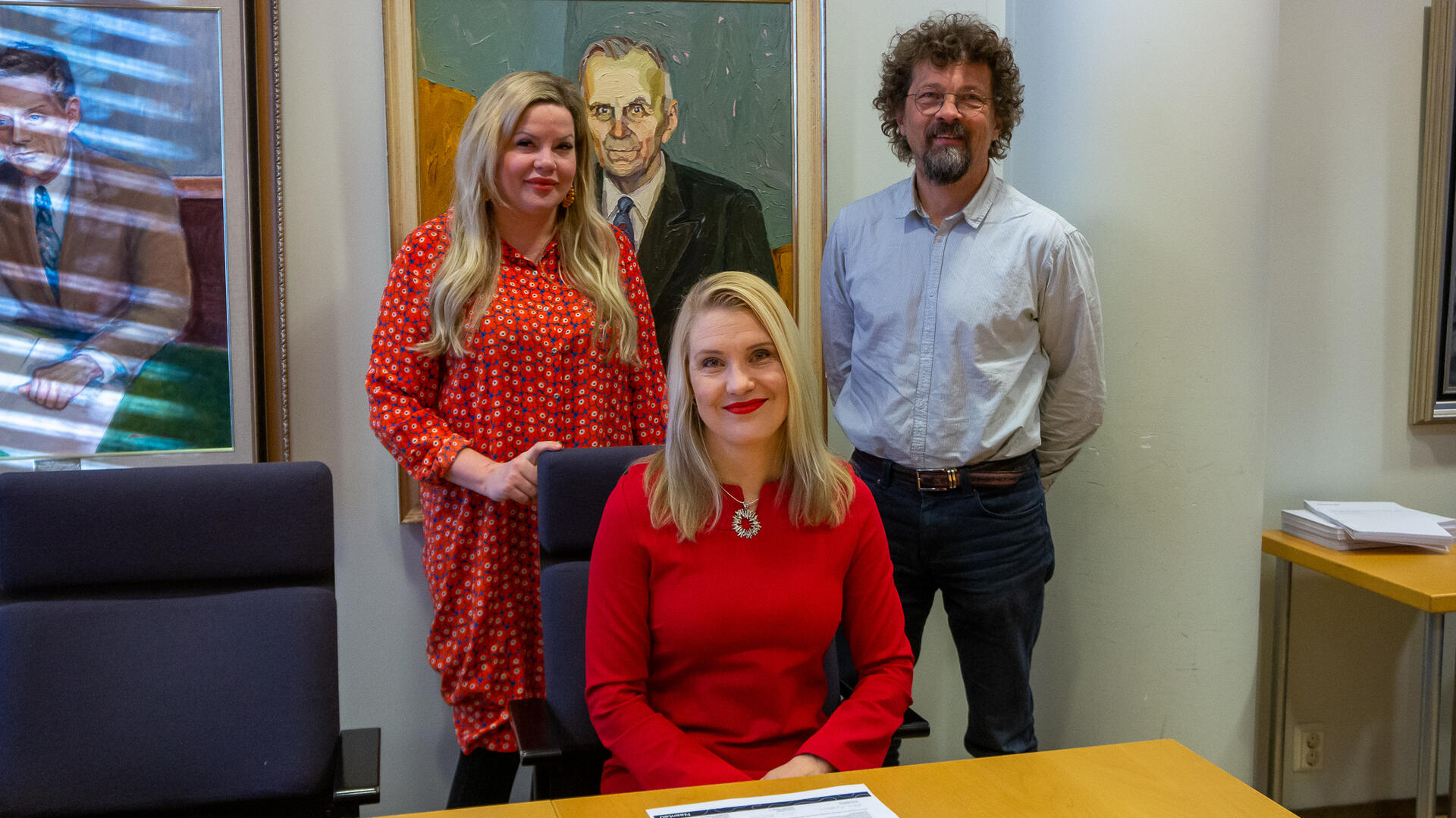 Laura Leppänen pöydän ääressä, takana seisovat Annika Virtanen ja Lassi Lähteenmäki.