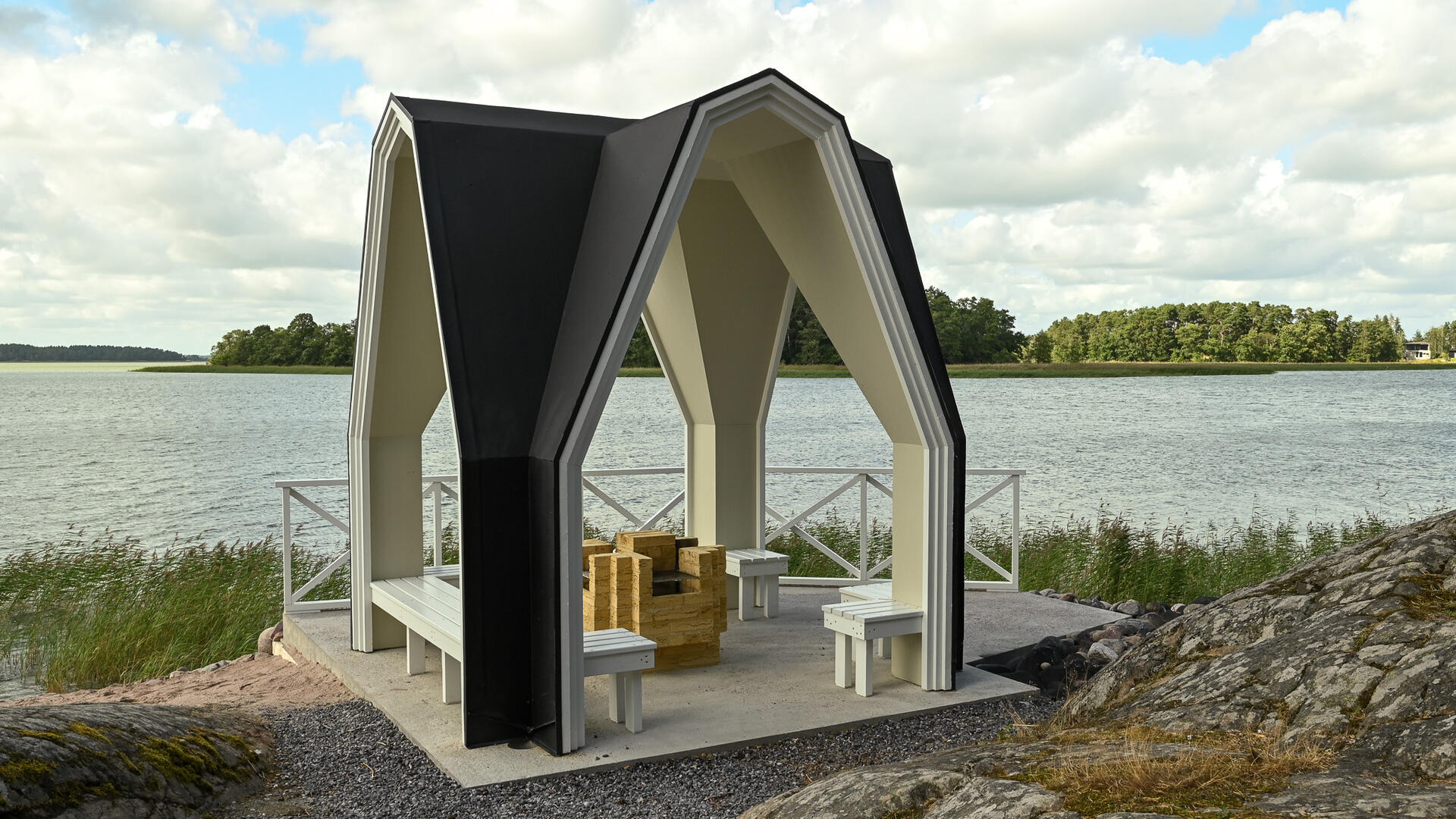 Nunnalahden avoin kaarimuotoinen paviljonki, jonka keskellä on grillauspaikat ja reunalla istuimia.