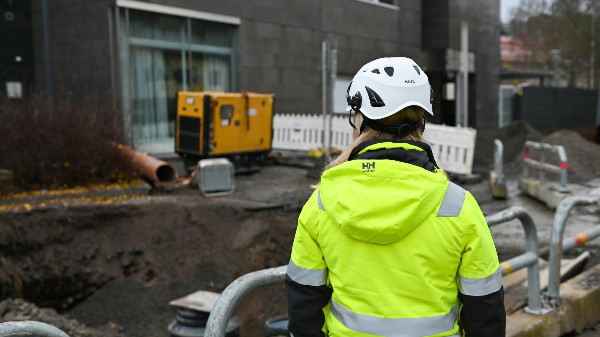 Työnjohtaja keltaisessa huomiotakissa valvoo työmaata Naantalissa. Taustalla kaupungintalo.