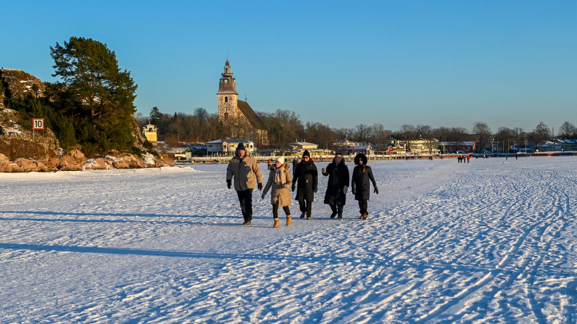 Ihmisiä kävelemässä meren jäillä Naantalissa. Taustalla vierasvenesatama ja kirkko.