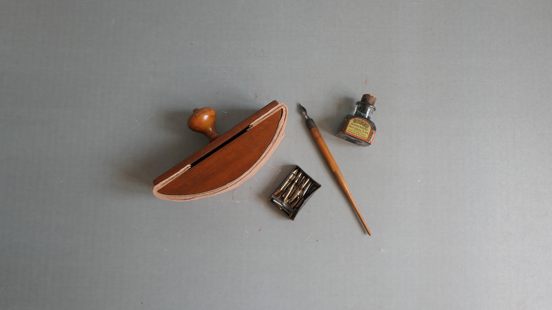 harmaalla pohjalla vanha mustekynä vaihtoterineen, mustekuivain ja mustepullo 