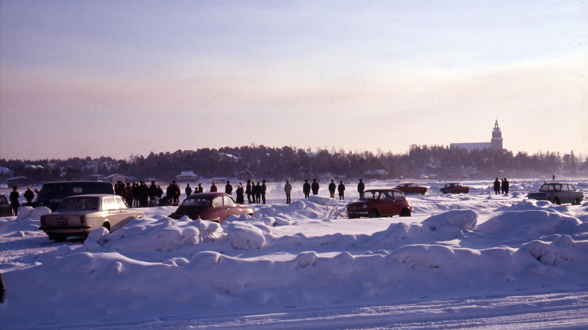 Meren jäällä autoja ja yleisöä, rannalla asuinrakennuksia ja Naantalin kirkko