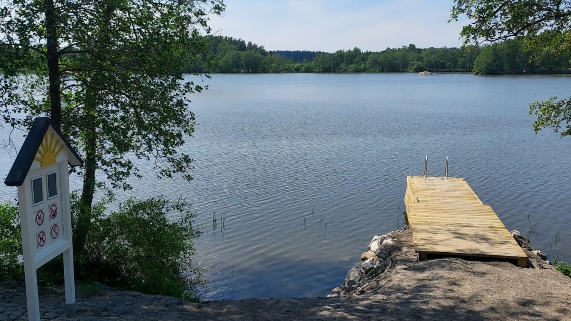 Laituri järven rannalla, vasemmalla kyltti uimapaikasta.