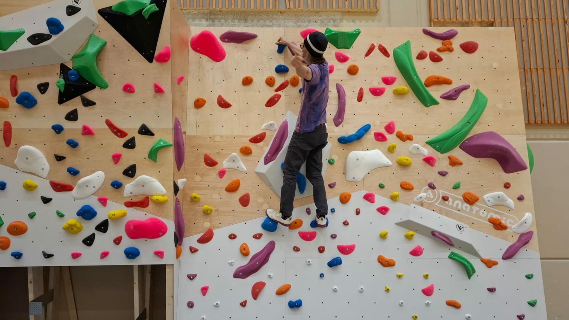Henkilö boulderointiseinällä, jossa eri värisiä ulokkeita, joista voi ottaa kiinni.