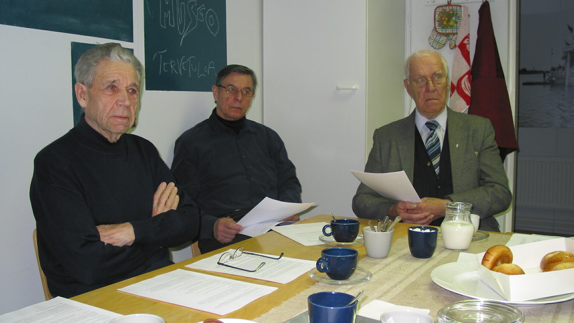 kolme miestä pöydän ympärillä