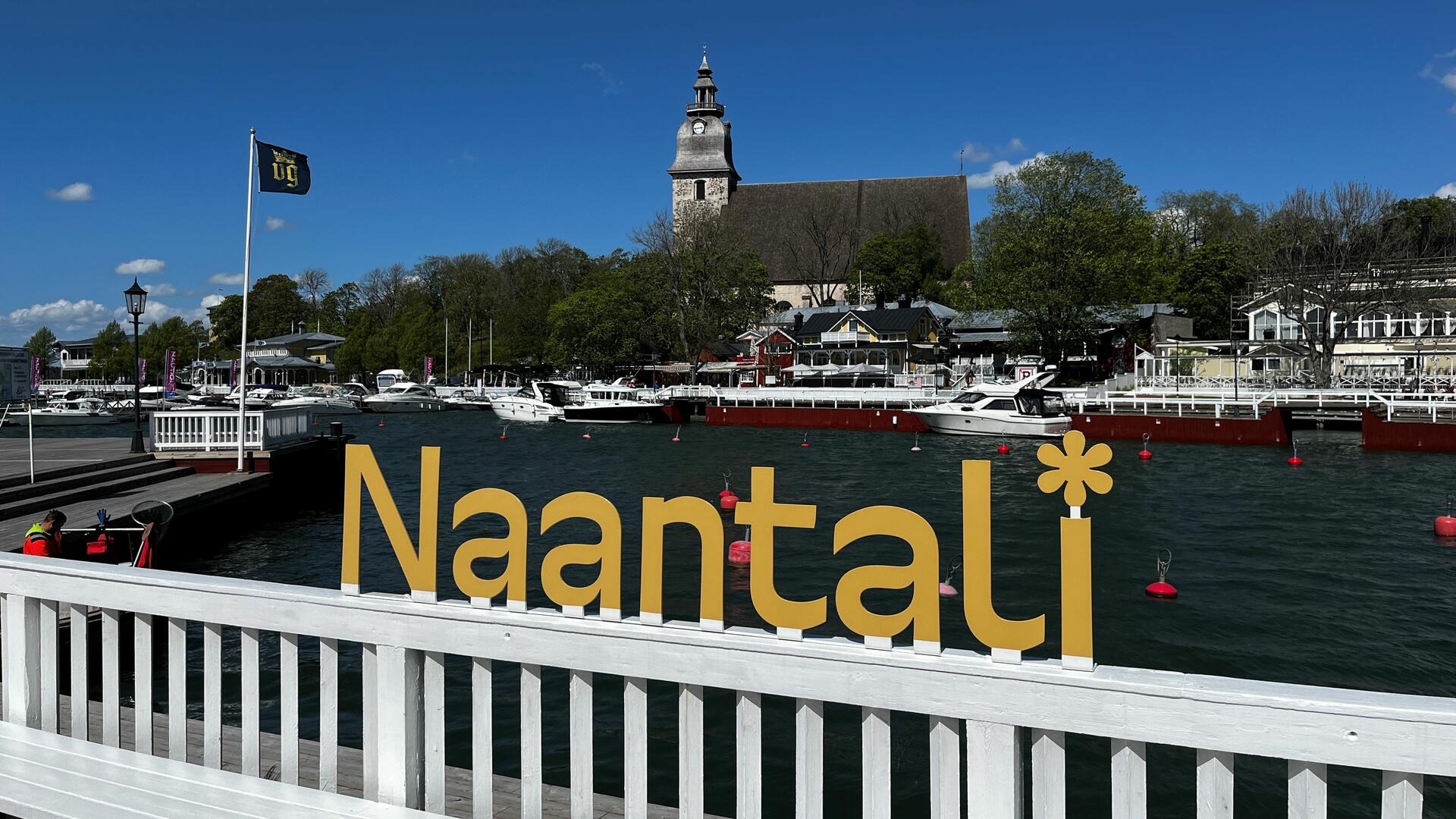 Naantalin rannassa keltaiset logon mukaiset Naantali-kohokirjaimet ja taustalla Naantalin kirkko.