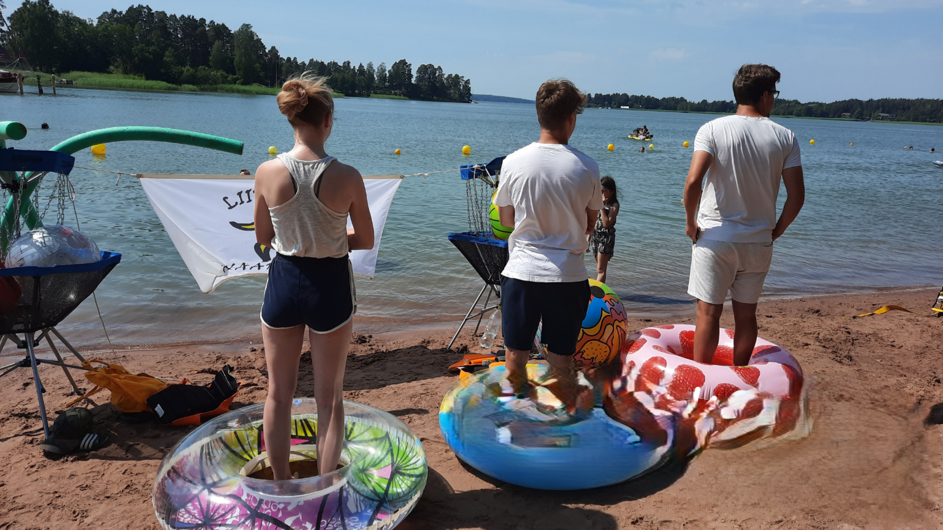 Kolme nuorta seisoo rannalla uimarenkaissa