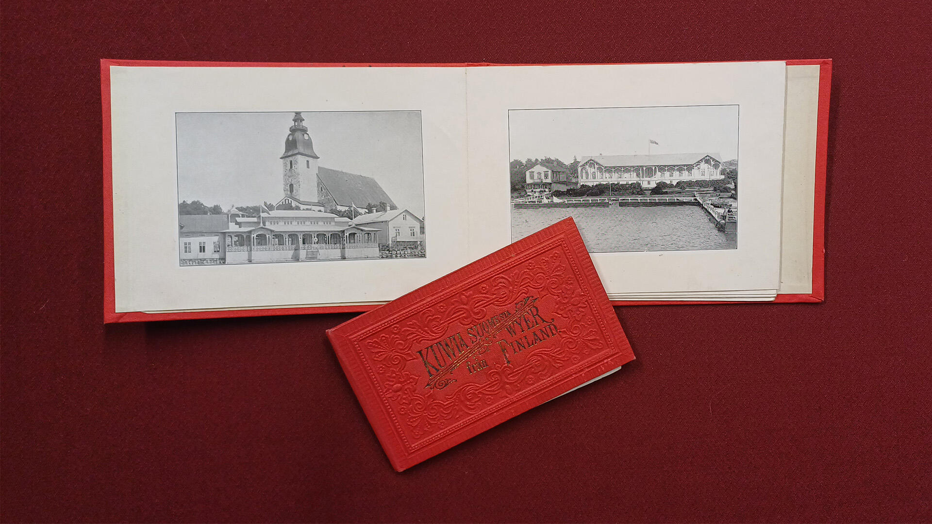 Punaisella taustalla avoin vihkonen, jossa kaksi mustavalkoista valokuvaa
