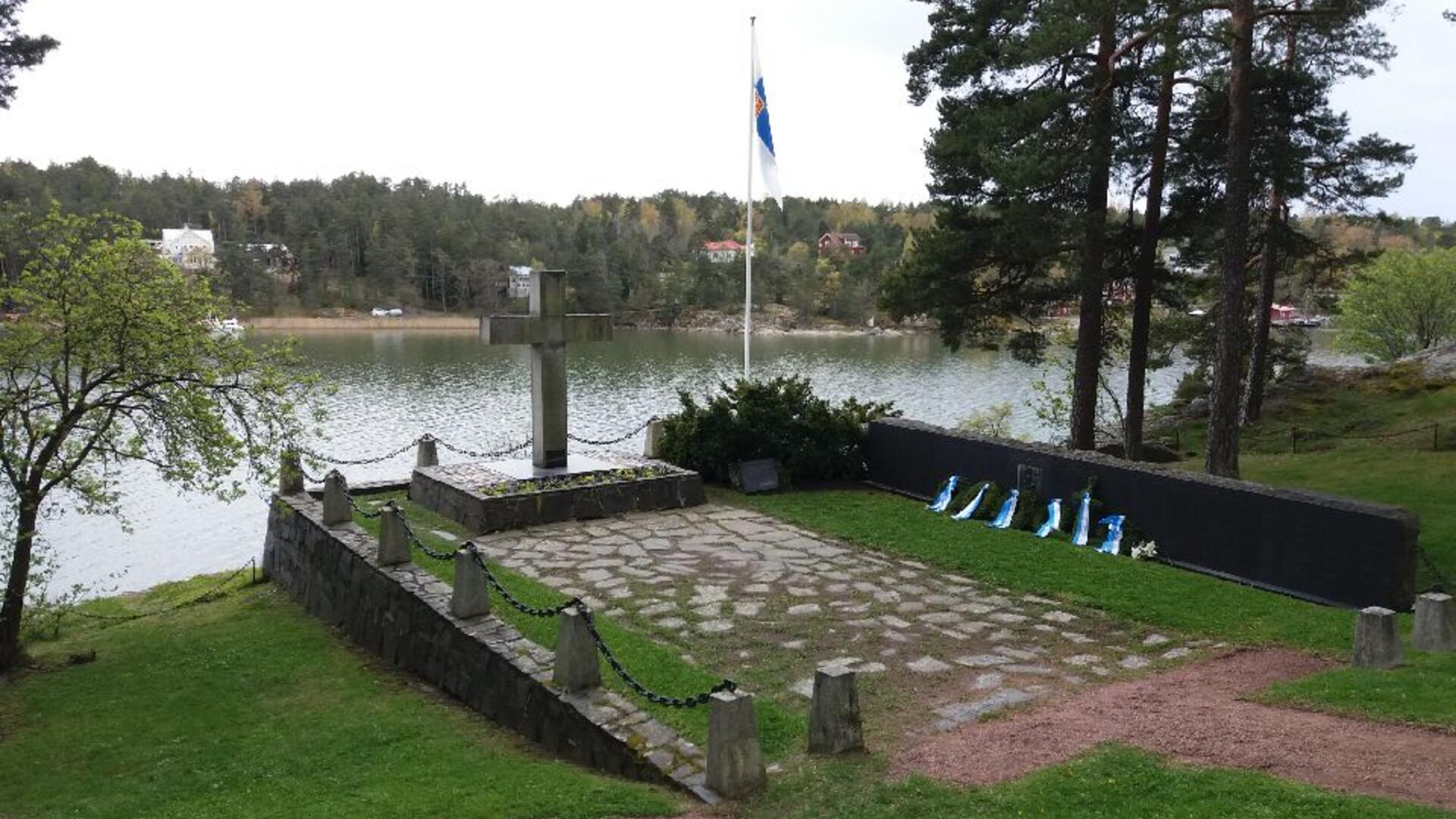 Kivinen muistomerkki, lipputanko ja muistoseinä meren rannalla.