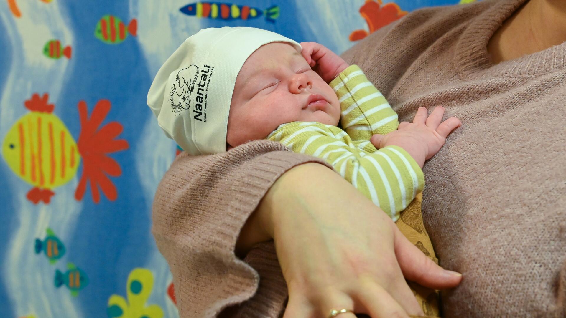 Vuoden 2025 ensimmäinen vauva Muumipipo päässä, äitinsä sylissä.