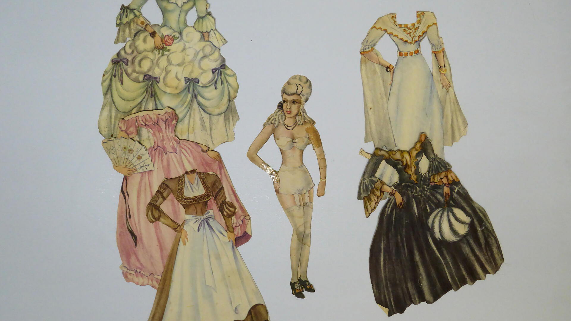 keskellä naispaperinukke ja kummallakin puolella paperista irti leikattuja vaatteita