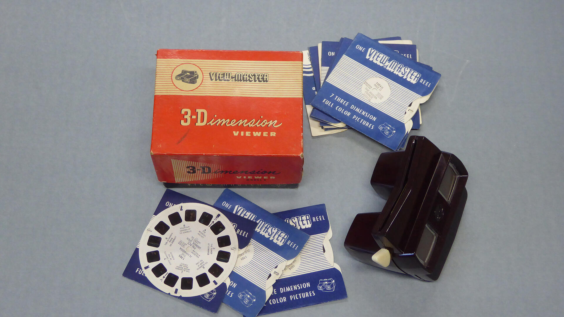 harmaalla taustalla musta view master -laite, sen pahvinen kotelo ja kuvakiekkoja 