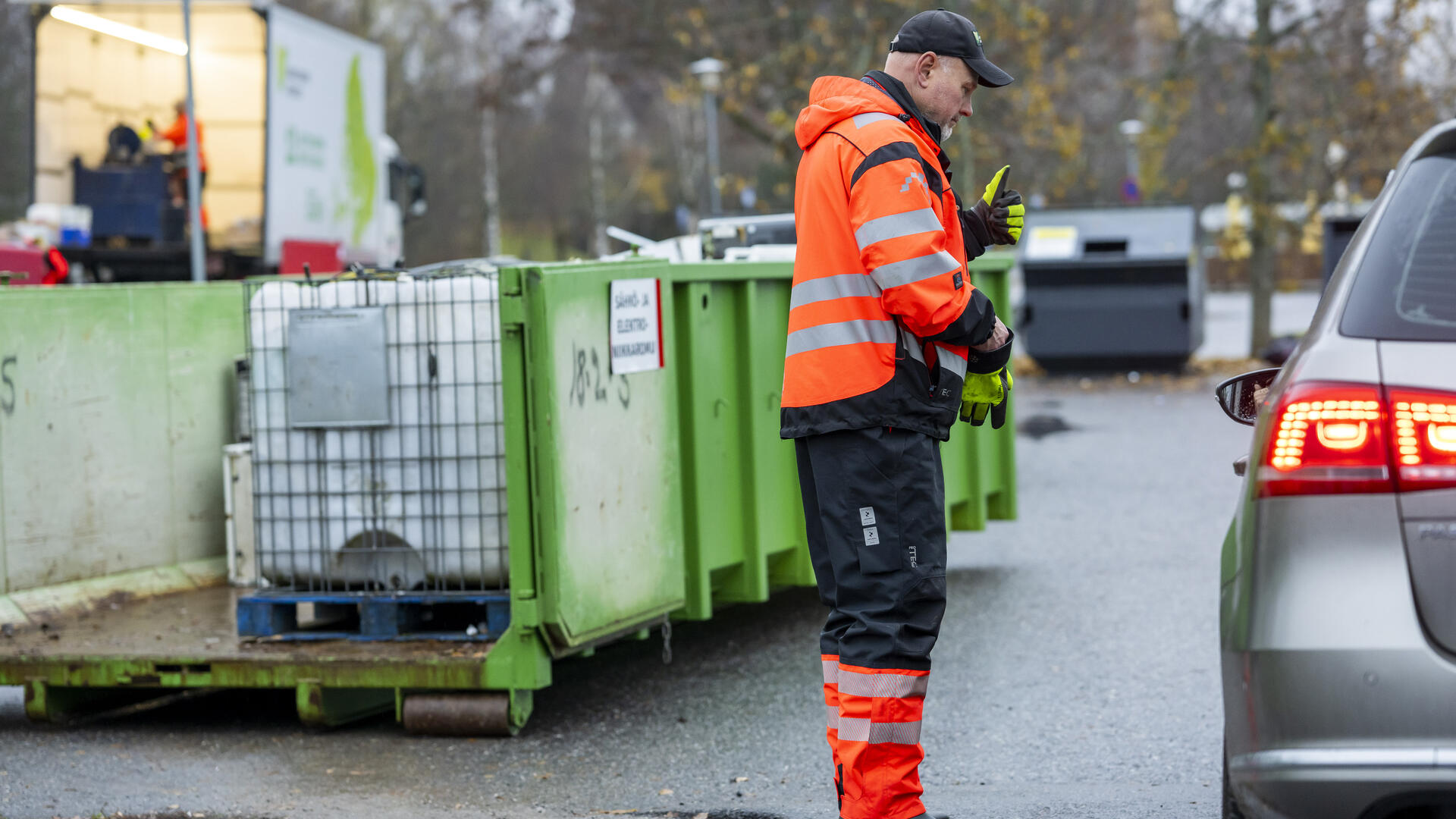 Liikkuvan lajitteluaseman työntekijä kääntyneenä autoon päin, taustalla jätelava.