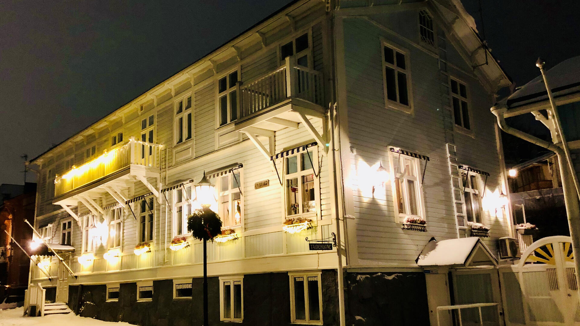 Vaaleanvihreä puurakennus valaistuna keskellä pimeyttä. Maassa on lunta.