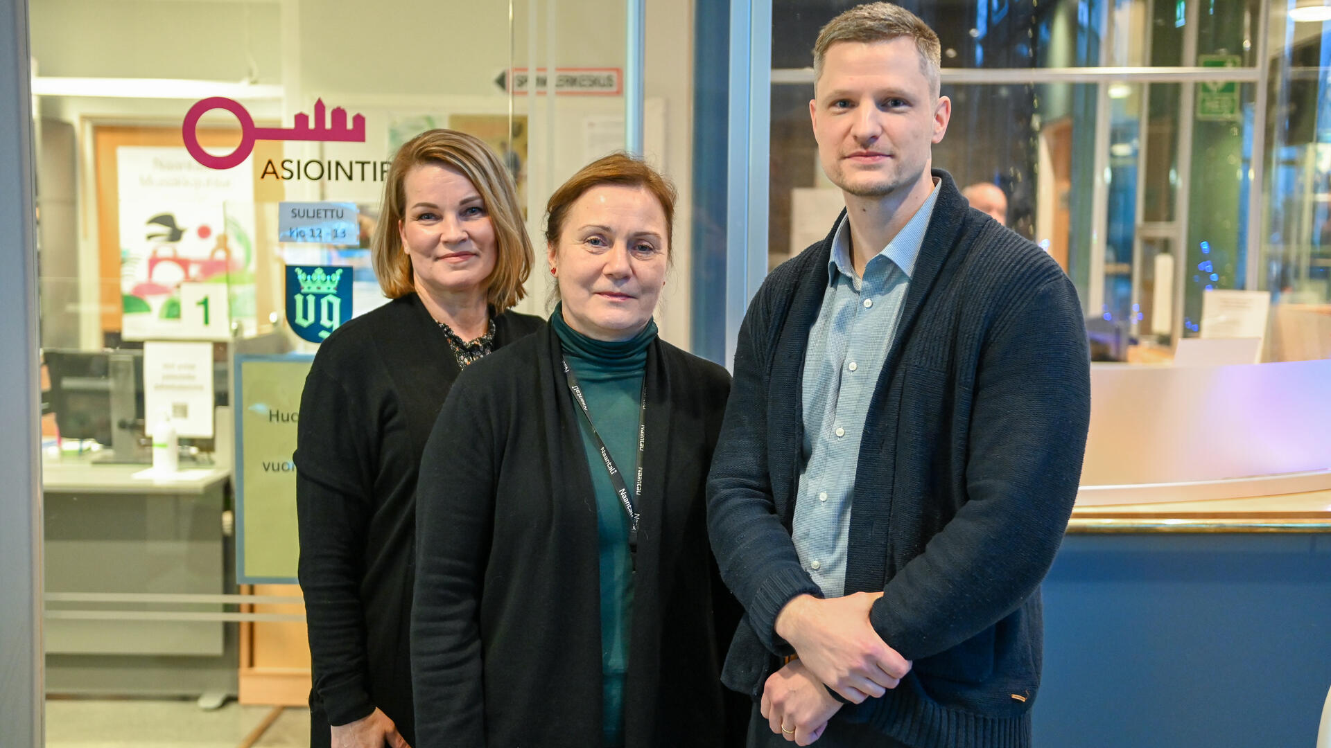 Kolme henkilöä kaupungin palvelupisteen edessä