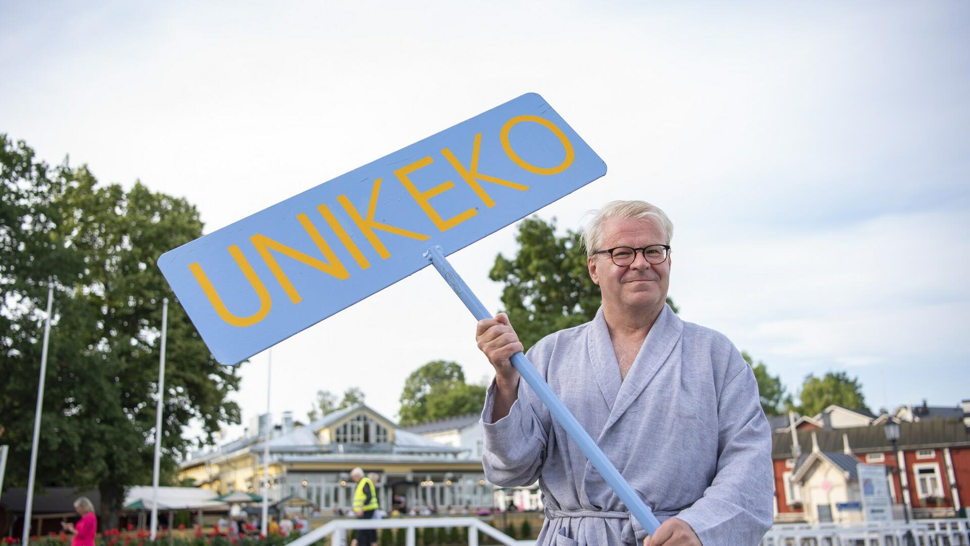 Kaupunginjohtaja Jouni Mutanen pitelee Unikeko-kylttiä kylpytakki päällä.