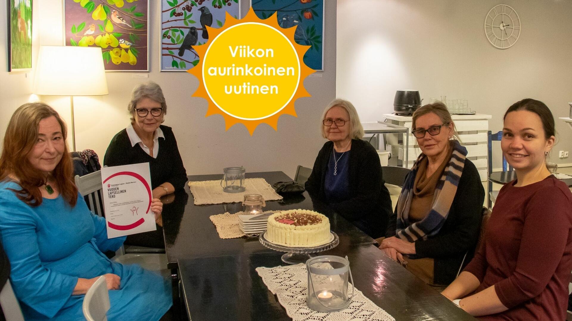 Kahvilan pöydän ympärillä istuu viisi naista katsoen kameraan. Siniseen mekkoon pukeutunut pitkähiuksinen nainen pitelee diplomia. Viikon aurinkoinen uutinen -logo.
