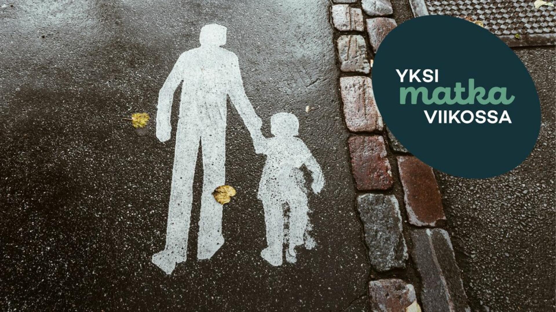 Asfalttiin on maalattu kävelytien merkki, jossa aikuinen ja lapsi kävelevät käsi kädessä.